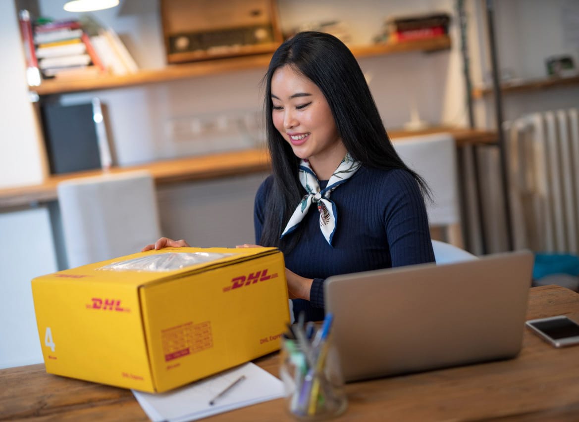 A woman sitting in front of her computer preparing a DHL parcel for international shipping